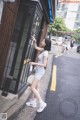 A woman standing in front of a phone booth on the street.