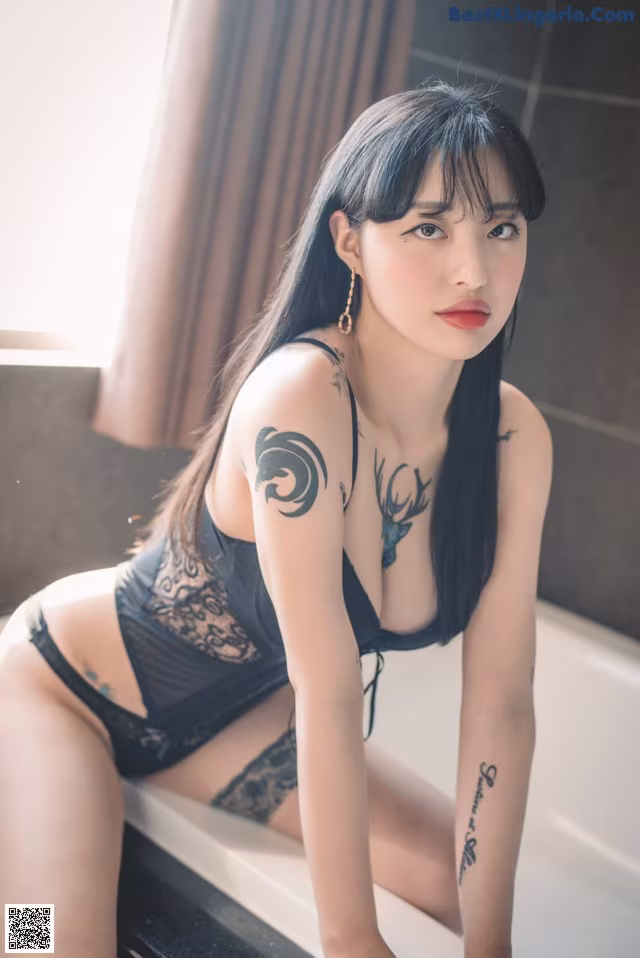 A woman sitting in a bathtub with a tattoo on her arm.