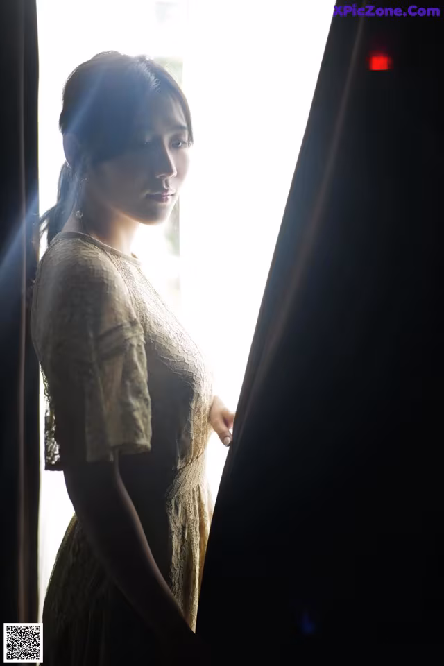 A woman standing in front of a window looking out the window.