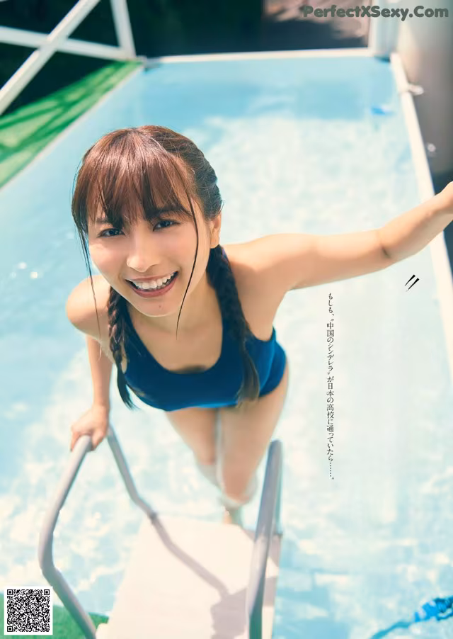 A woman in a blue bathing suit standing next to a swimming pool.