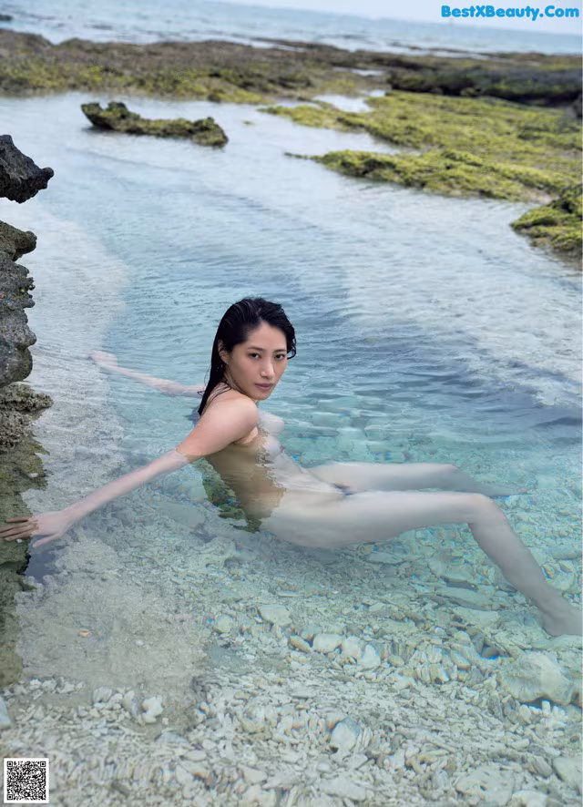 A naked woman is sitting in the water. 