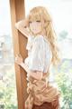 A girl with long blonde hair leaning against a wooden pole.