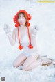 A woman in a white dress and red hat sitting in the snow.