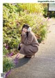 A woman crouching down in front of a bush of purple flowers.