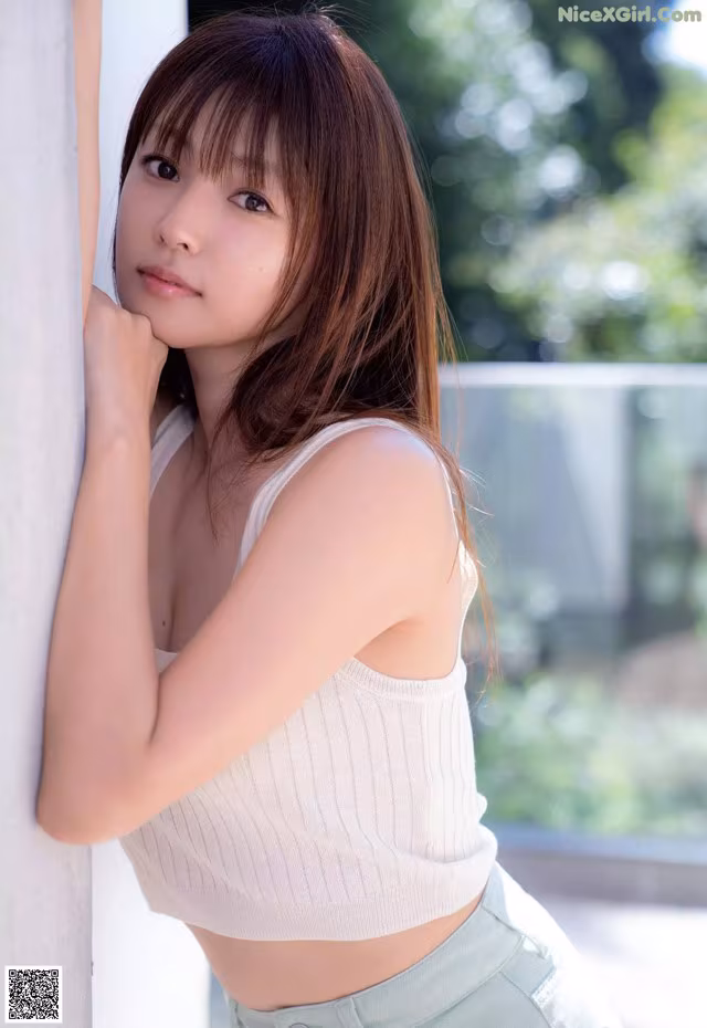 A young woman leaning against a wall with her hand on her chin.