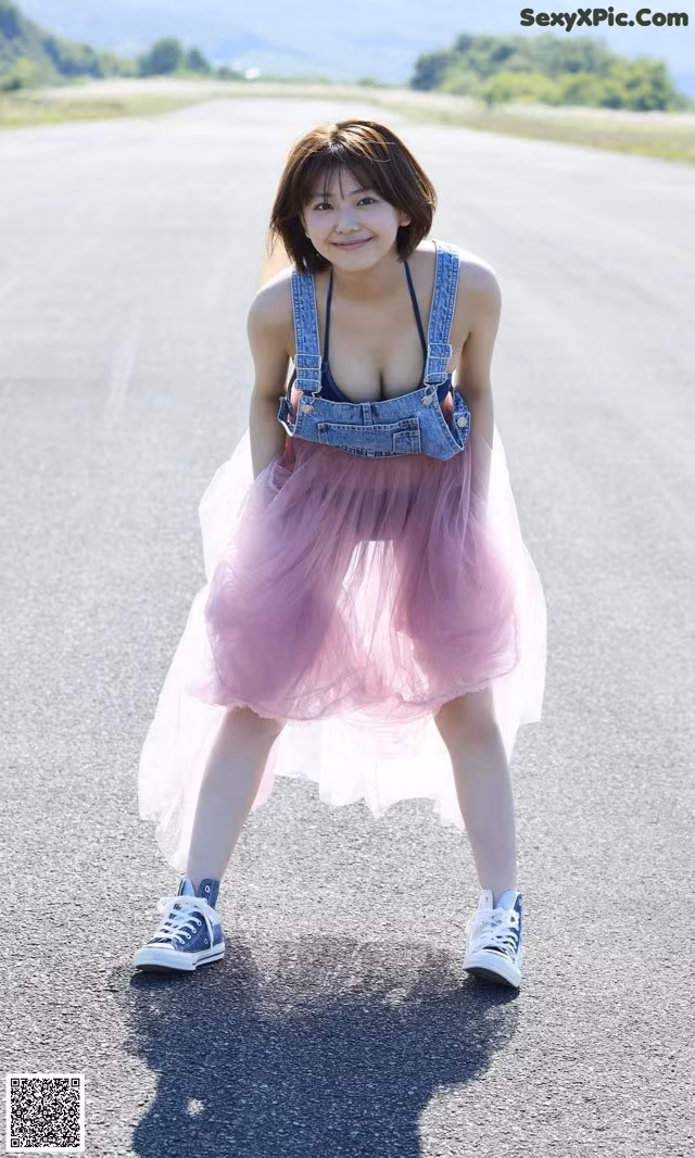 A woman in a pink tulle skirt and denim overalls posing on a road.