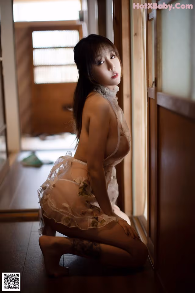 A woman in lingerie sitting on the floor in front of a door.