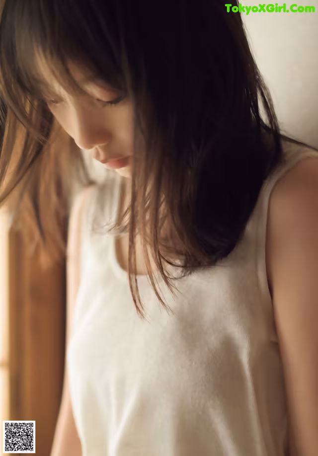 A woman in a white tank top looking out a window.